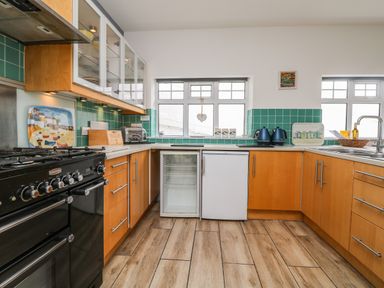 A kitchen with wooden cabinets black oven turquoise tile backsplash and two windows at Trelawns in Mawgan Porth
