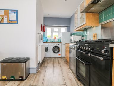 A kitchen with a black stove dishwasher washing machine dryer and trash bin at Trelawns in Mawgan Porth