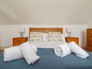 A bedroom with a wooden bed frame two bedside tables with lamps and rolled white towels on the blue bedspread at Trelawns in Mawgan Porth