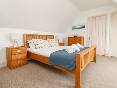 A bedroom with a wooden bed, bedside tables with lamps, a chest of drawers, and doors at Trelawns in Mawgan Porth
