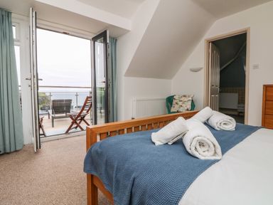 A bedroom with a bed with towels on top and open doors leading to a balcony with chairs at Trelawns in Mawgan Porth