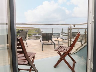A balcony with wooden chairs and lounge chairs overlooking the ocean at Trelawns in Mawgan Porth