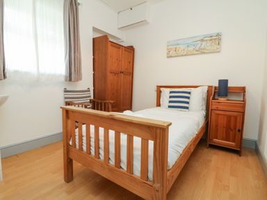 A bedroom with a wooden single bed a bedside table with a lamp a wooden wardrobe and a chair at Trelawns in Mawgan Porth
