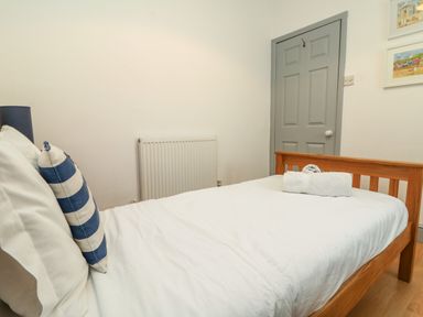 A bedroom with a wooden bed white linens striped pillow gray door and framed pictures at Trelawns in Mawgan Porth