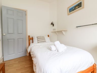 A bedroom with a single bed with white bedding towels on bed wooden door and framed picture on wall at Trelawns in Mawgan Porth