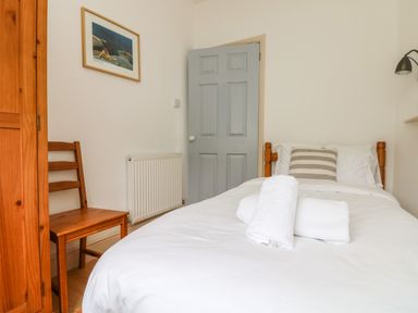 A bedroom with a single bed with white bedding and towel on top next to a wooden chair and wardrobe with a gray door at Trelawns in Mawgan Porth