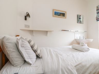A bedroom with a bed pillows and folded towels next to a wall mounted sink at Trelawns in Mawgan Porth
