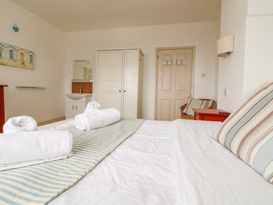 A bedroom with a bed with striped pillows and towels on it a wardrobe a door a washbasin and a chair at Trelawns in Mawgan Porth