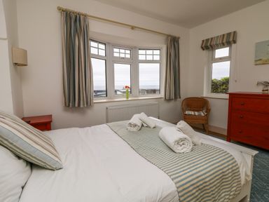 A bedroom with a bed and rolled towels with striped curtains on windows and a red dresser at Trelawns in Mawgan Porth