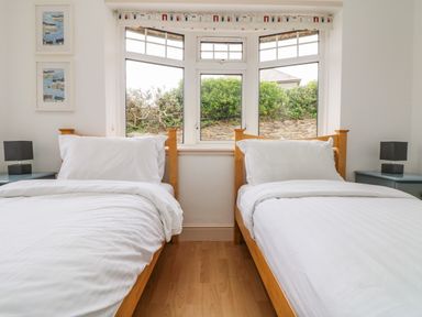 A bedroom with two single beds with white bedding and wooden frames and a window between them at Trelawns in Mawgan Porth