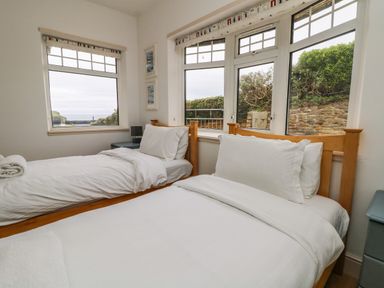A bedroom with two single beds and windows showing greenery outside at Trelawns in Mawgan Porth