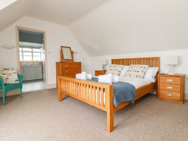 A bedroom with a wooden bed and matching bedside tables with lamps and a chest of drawers at Trelawns in Mawgan Porth