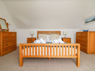 A bedroom with a wooden bed frame, bedside tables with lamps, dressers, and a mirror at Trelawns in Mawgan Porth