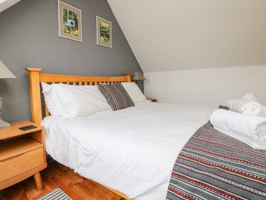 A bedroom with a wooden bed frame white bedding a striped blanket and two framed pictures on a gray wall at Trelawns in Mawgan Porth
