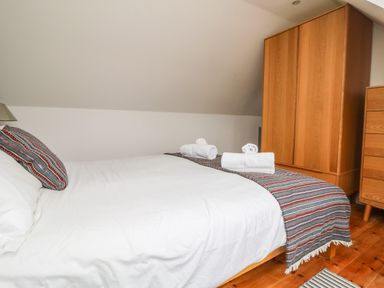 A bedroom with a bed folded towels on a striped runner wooden wardrobe and chest of drawers at Trelawns in Mawgan Porth