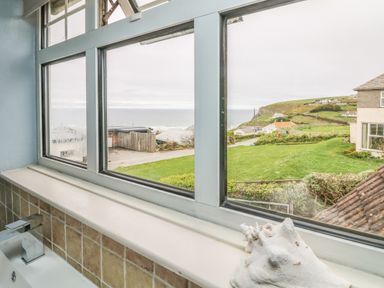 A window with a view of the sea hills and houses above a sink in a bathroom at Trelawns in Mawgan Porth