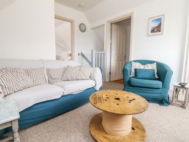 A living room with a teal sofa and armchair with striped cushions and a cable spool coffee table at Trelawns in Mawgan Porth
