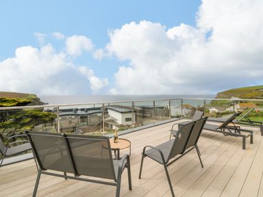A balcony with chairs and a table overlooking the sea and nearby buildings at Trelawns in Mawgan Porth