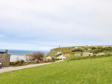 A grassy area with houses on a hill and the sea in the background at Trelawns in Mawgan Porth