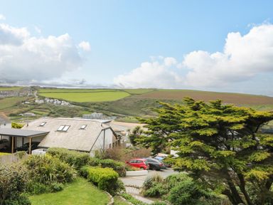 A residential area with houses cars and green hills under a blue sky at Trelawns in Mawgan Porth