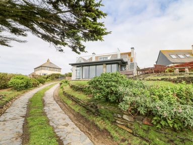 A stone driveway leading to a house with a glass extension and garden seating at Trelawns in Mawgan Porth