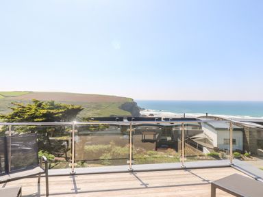 A balcony with glass railing overlooking the ocean and green hills at Trelawns in Mawgan Porth