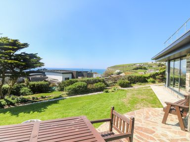 A garden with wooden outdoor furniture overlooking the sea and hills at Trelawns in Mawgan Porth