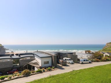 A building with parked vans near a coastline with ocean and cliffs at Trelawns in Mawgan Porth