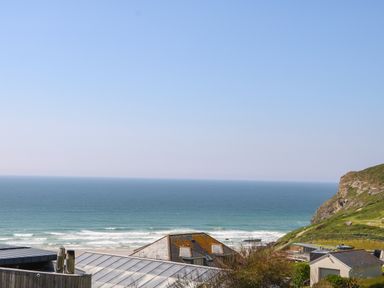 A view of the ocean with waves and rooftops of buildings near a hillside at Trelawns in Mawgan Porth