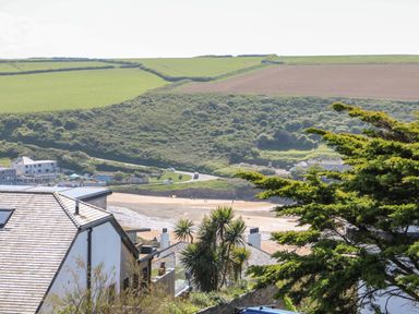 A coastal view with houses trees a sandy beach and green fields at Trelawns in Mawgan Porth