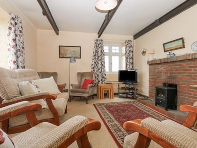 A living room with armchairs a sofa carpet brick fireplace television and floral curtains at Parc An Castle Cottage in Lizard