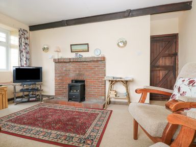A living room with a brick fireplace television floral curtains and armchairs at Parc An Castle Cottage in Lizard