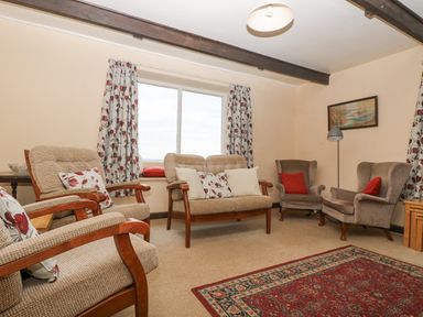 A living room with armchairs a sofa a floor lamp a framed picture and patterned curtains at Parc An Castle Cottage in Lizard