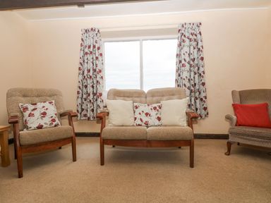 A sitting room with two armchairs and a two-seater sofa with cushions in front of a window with floral curtains at Parc An Castle Cottage in Lizard