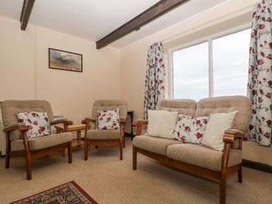 A sitting room with sofa and armchairs with floral cushions and a large window with floral curtains at Parc An Castle Cottage in Lizard