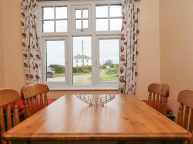 A wooden dining table with four wooden chairs near a window with patterned curtains at Parc An Castle Cottage in Lizard