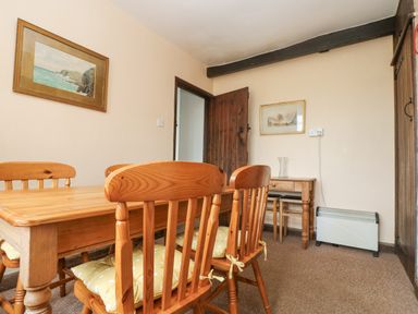 A dining room with wooden table and chairs and framed pictures on the wall at Parc An Castle Cottage in Lizard