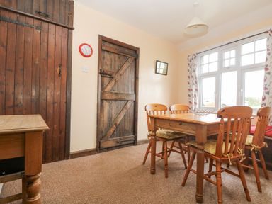 A dining room with a wooden table and four chairs next to a window with patterned curtains at Parc An Castle Cottage in Lizard