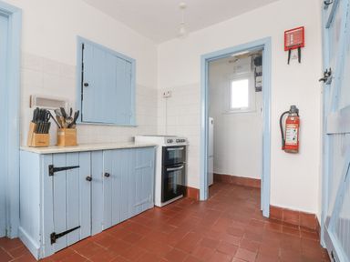 A kitchen with blue cabinets a stove a knife block a fire extinguisher and a door opening to another room at Parc An Castle Cottage in Lizard