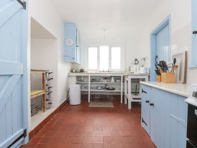 A kitchen with blue cabinets a trash bin and pots and pans on open shelves at Parc An Castle Cottage in Lizard