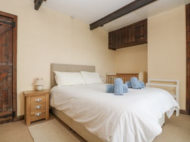 A bedroom with a bed white bedding blue towels wooden crib wooden doors and beige walls at Parc An Castle Cottage in Lizard