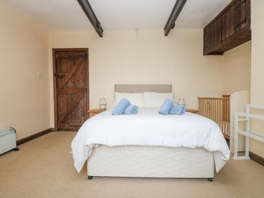 A bedroom with a double bed with white bedding and blue towels a wooden door and a baby crib at Parc An Castle Cottage in Lizard