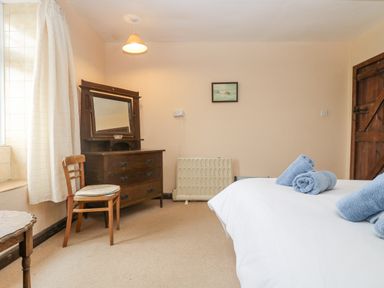 A bedroom with a wooden chair a dresser with a mirror a bed with blue towels and a wooden door at Parc An Castle Cottage in Lizard