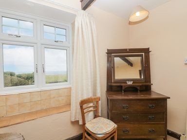 A room with a window with curtains a wooden chair and a wooden dresser with a mirror at Parc An Castle Cottage in Lizard