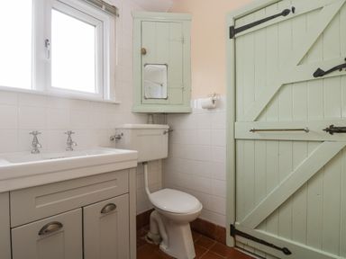 A bathroom with a toilet a sink with faucets a window a wall cabinet with a mirror and a wooden door at Parc An Castle Cottage in Lizard