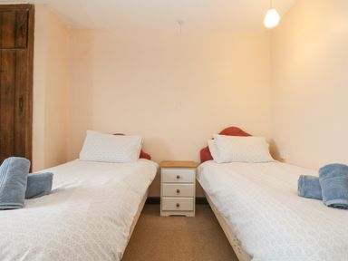 A bedroom with two single beds with white bedding and blue towels on each bed and a small white bedside table between the beds at Parc An Castle Cottage in Lizard
