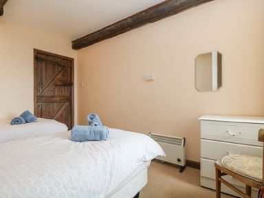 A bedroom with two single beds with towels on them a wooden door a heater a white chest of drawers and a wooden chair at Parc An Castle Cottage in Lizard