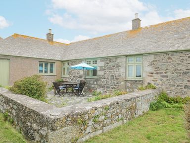A stone cottage exterior with a small patio area containing a table with umbrellas and chairs at Parc An Castle Cottage in Lizard