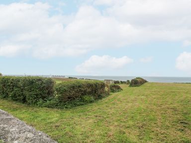 A grassy field with trimmed hedges and a view of the sea at Parc An Castle Cottage in Lizard