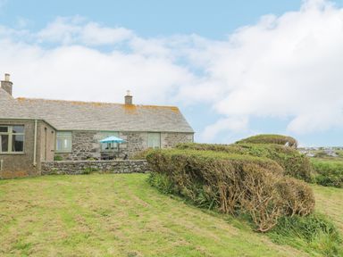 A stone cottage with a slate roof and green windows with a garden and bushes in front at Parc An Castle Cottage in Lizard